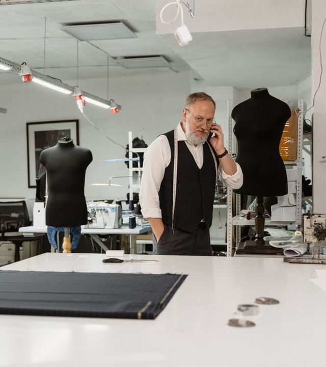 Un artisan tailleur, au téléphone dans son atelier, devant une table de coupe